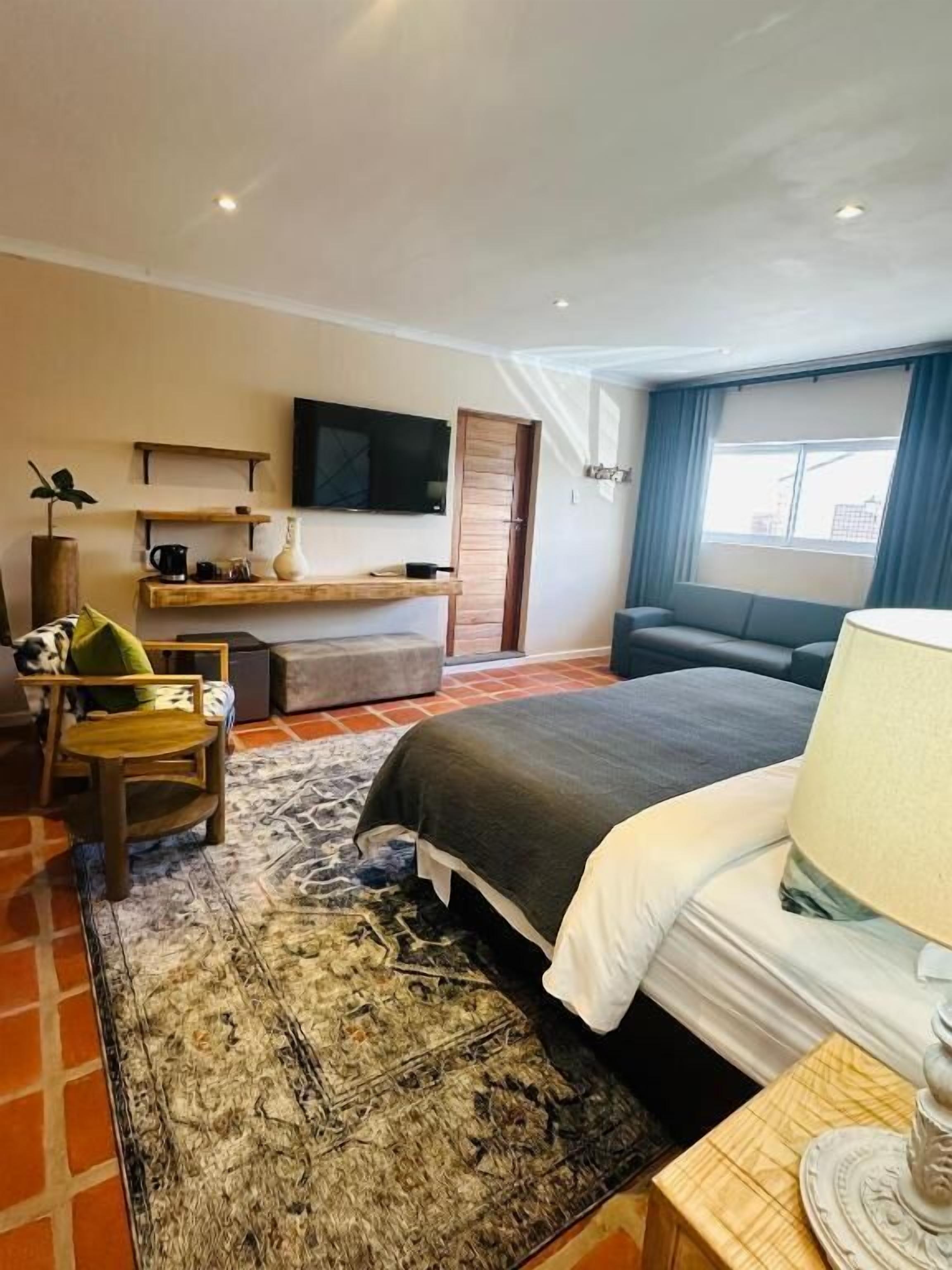 A hotel room with a bed, a desk, a chair, a TV, and a window with curtains.