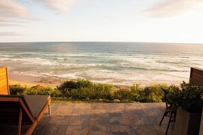 Un patio con vistas al océano, a una playa y una terraza de madera.