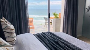Un dormitorio con una cama grande, vistas al océano y un balcón con mesa y sillas.