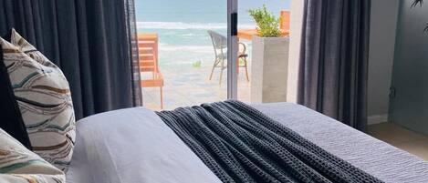 Een slaapkamer met een groot bed, uitzicht op de oceaan en een balkon met een tafel en stoelen.