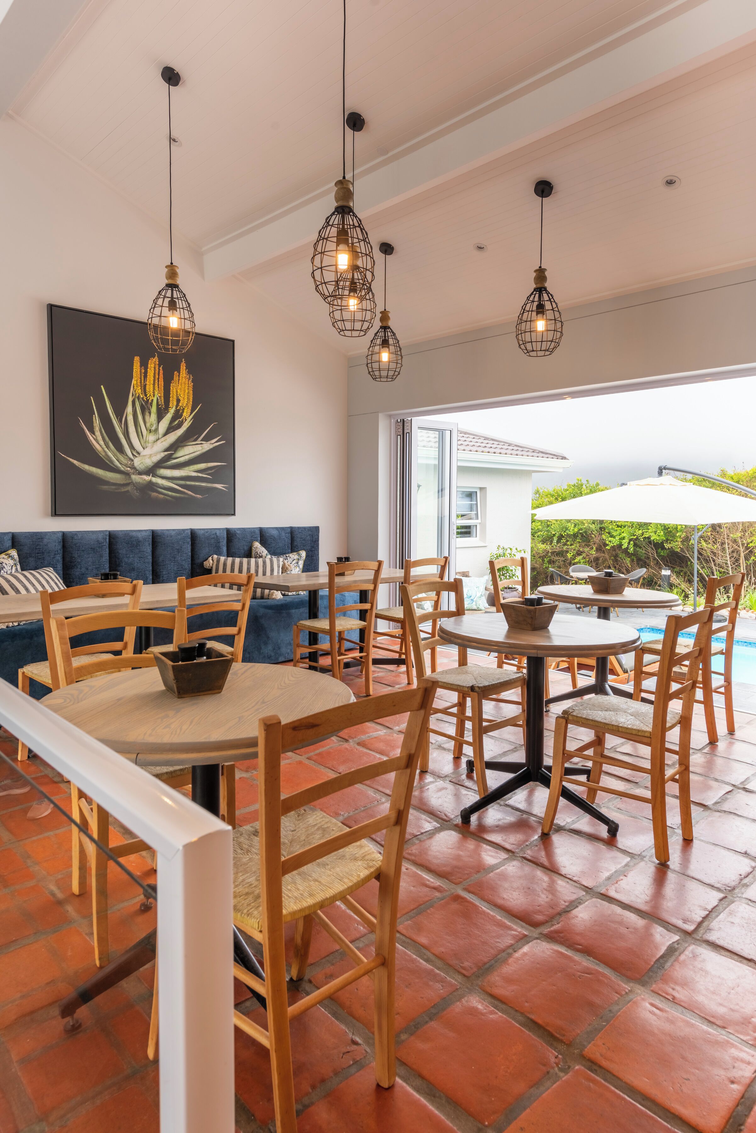 A dining area with wooden chairs and tables, a blue sofa, and pendant lighting.