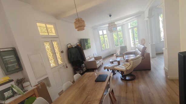 Ein geräumiges Wohnzimmer mit einem Holzesstisch, Ledersofas und einem großen Fenster mit Tageslicht.