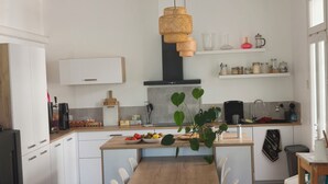 Eine moderne Küche mit weißen Schränken, einem Holztisch und einer hängenden Rattan-Leuchte.