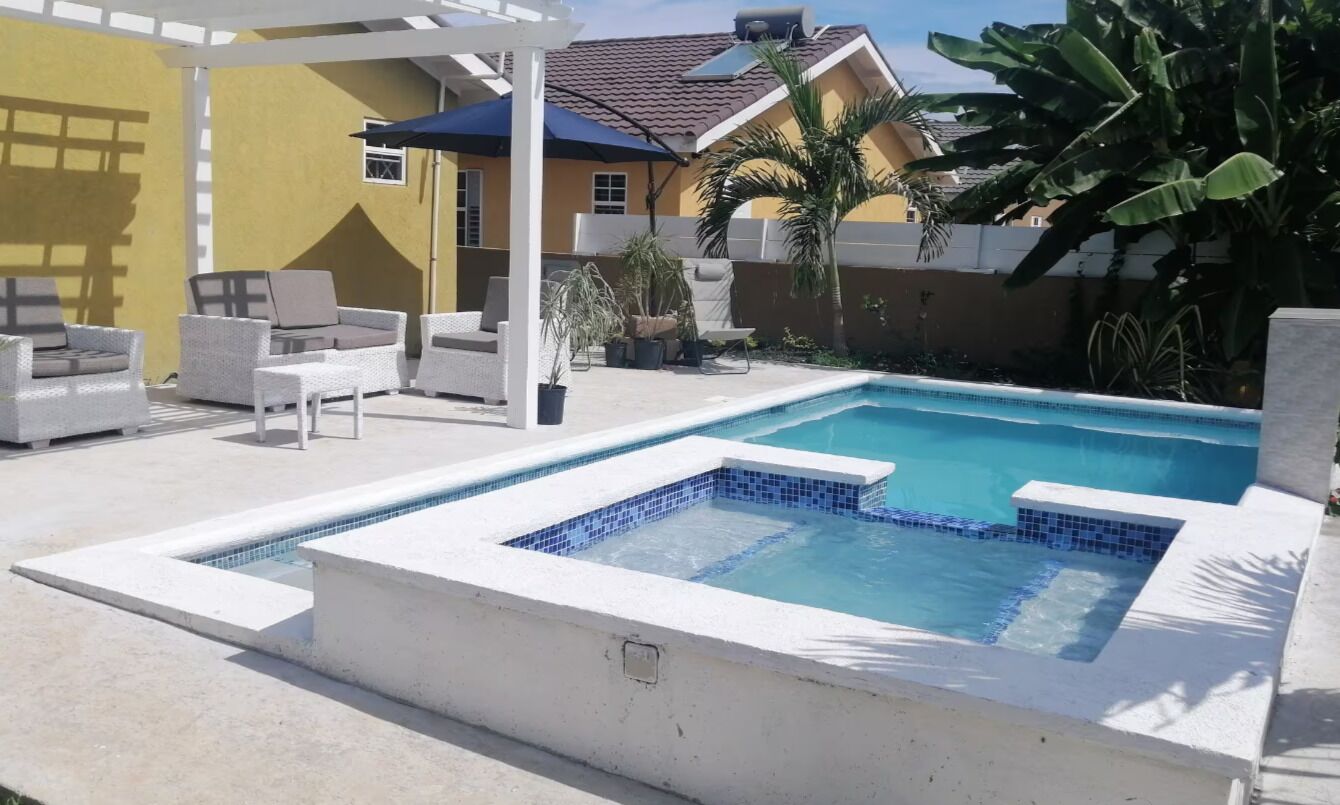 A swimming pool with a white deck, lounge chairs, and a pergola.