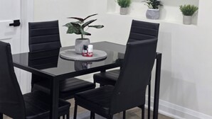 A dining area with a black table, four chairs, a potted plant, and a shelf with various plants.