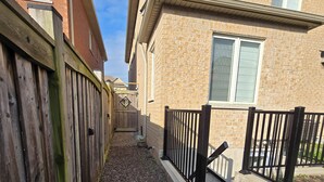 A residential area with a wooden fence, gravel pathway, and a house with a brick exterior and windows.