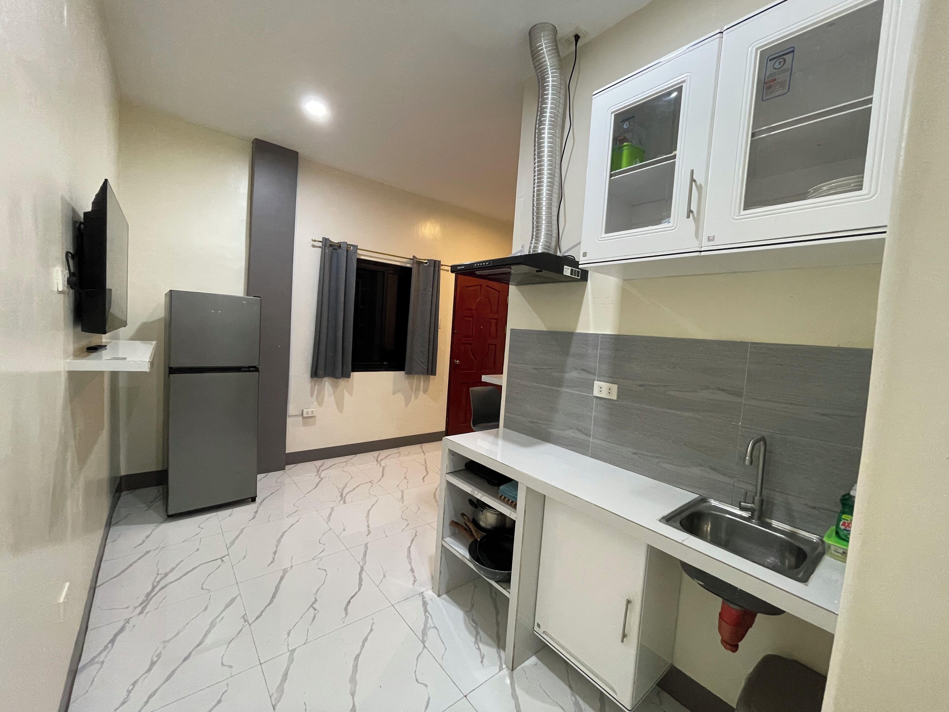 A compact kitchen with a refrigerator, a sink, cabinets, and a ventilation system.
