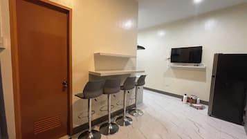 A compact kitchen with a refrigerator, a TV mounted on the wall, and a bar area with stools.
