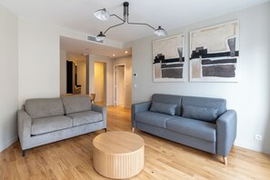 Een moderne woonkamer met twee grijze banken, een houten salontafel en abstracte kunst aan de muren.