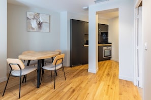 A dining area with a round table and four chairs, a kitchen with black cabinets and a built-in oven, and a hallway leading to another room. - Beautiful and Modern 1BDR Flat near Montmartre (Paris)