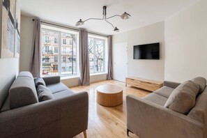 A modern living room with a sofa, a round wooden coffee table, and a TV mounted on the wall. - Beautiful and Modern 1BDR Flat near Montmartre (Paris)