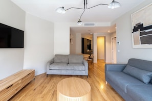 A modern living room with a grey sofa, a round wooden coffee table, and a flat-screen TV mounted on the wall. - Beautiful and Modern 1BDR Flat near Montmartre (Paris)