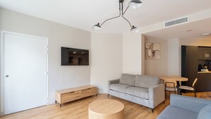 Ein modernes Wohnzimmer mit einem grauen Sofa, einem Holztisch und einem an der Wand befestigten Fernseher.