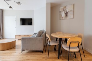 A modern living room with a flat-screen TV, a round wooden dining table with chairs, a grey sofa, and a wooden floor. - Beautiful and Modern 1BDR Flat near Montmartre (Paris)
