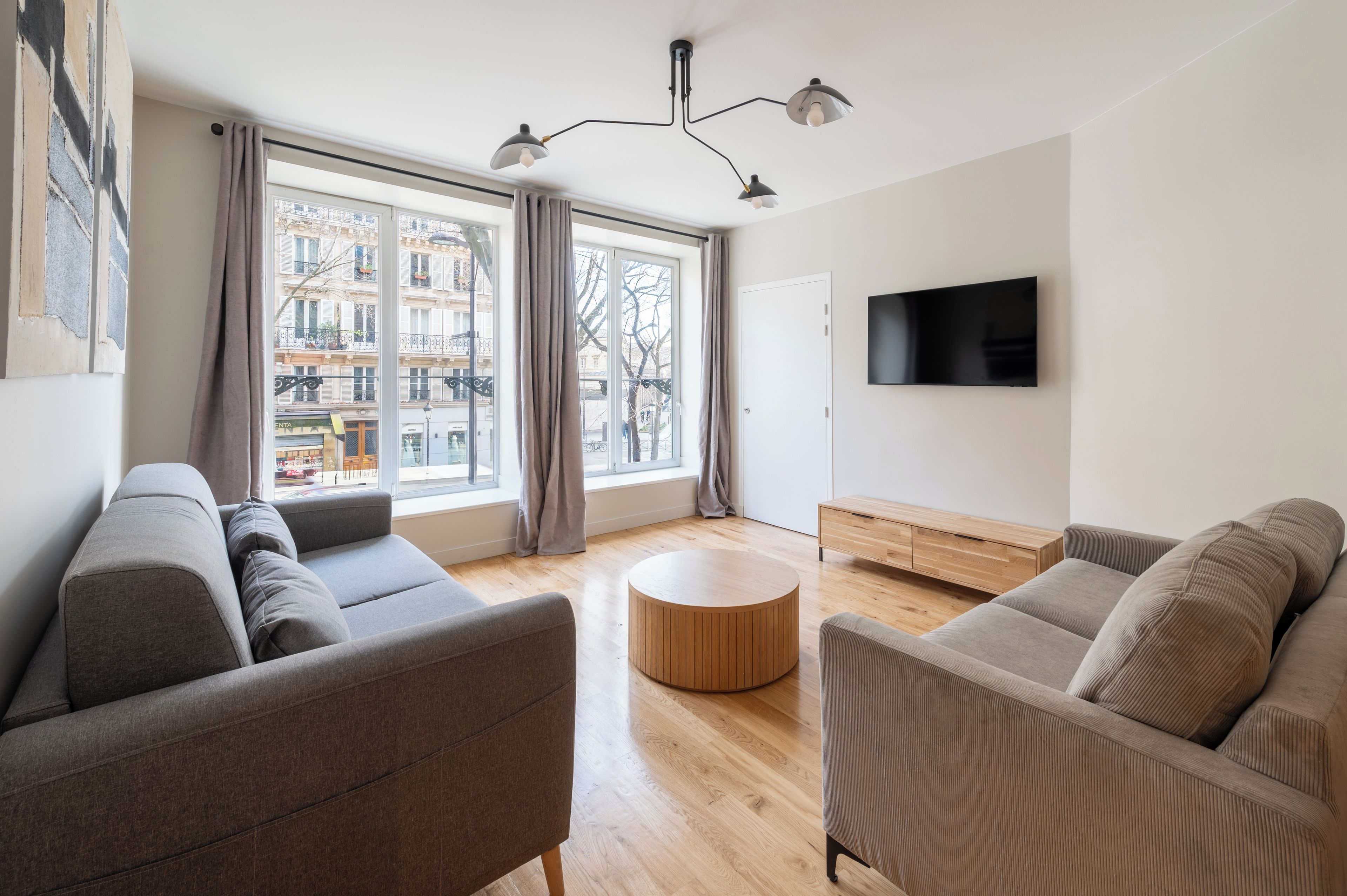 Ein modernes Wohnzimmer mit einer Couch, einem runden Holztisch und einem an der Wand befestigten Fernseher.