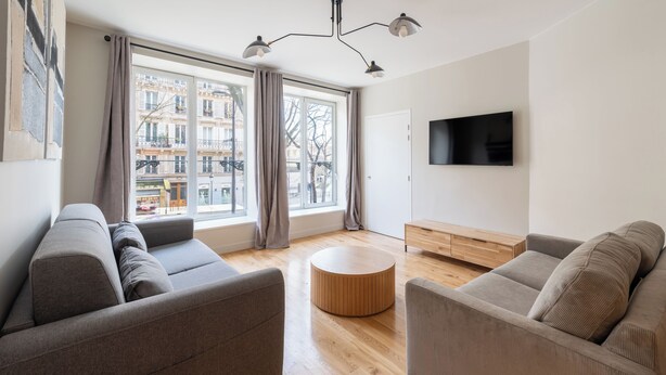 Ein modernes Wohnzimmer mit einer Couch, einem runden Holztisch und einem an der Wand befestigten Fernseher.