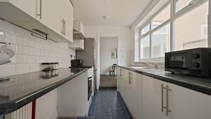 A modern kitchen with white cabinets, a black countertop, and a microwave. - Cleethorpes Home Near Beach, Free Parking, Fast (Cleethorpes)
