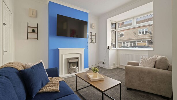 A living room with a blue accent wall, a fireplace, a sofa, a coffee table, and a TV. - Cleethorpes Home Near Beach, Free Parking, Fast (Cleethorpes)