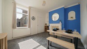 A room with a dining table, benches, a fireplace, a mirror, and a window with curtains. - Cleethorpes Home Near Beach, Free Parking, Fast (Cleethorpes)