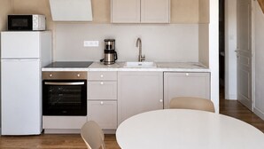 Una cocina moderna con armarios blancos, horno empotrado, cafetera y una mesa de comedor blanca con sillas.