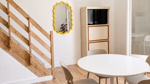 Un interior moderno con una escalera de madera, una mesa redonda blanca con sillas, un mueble para televisor y un espejo.