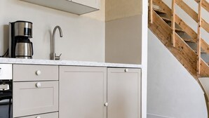 Una cocina con piso de madera, una cafetera y una escalera de madera.