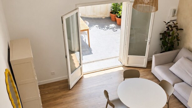Una sala moderna con piso de madera, una mesa redonda blanca y un sofá gris.