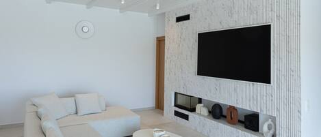 Una sala moderna con un sofá modular, un televisor de pantalla plana montado en una pared texturizada, un ventilador de techo y una mesa de centro.