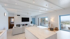 Uma sala de estar moderna com uma ilha grande, uma televisão de tela plana e vista para o exterior.