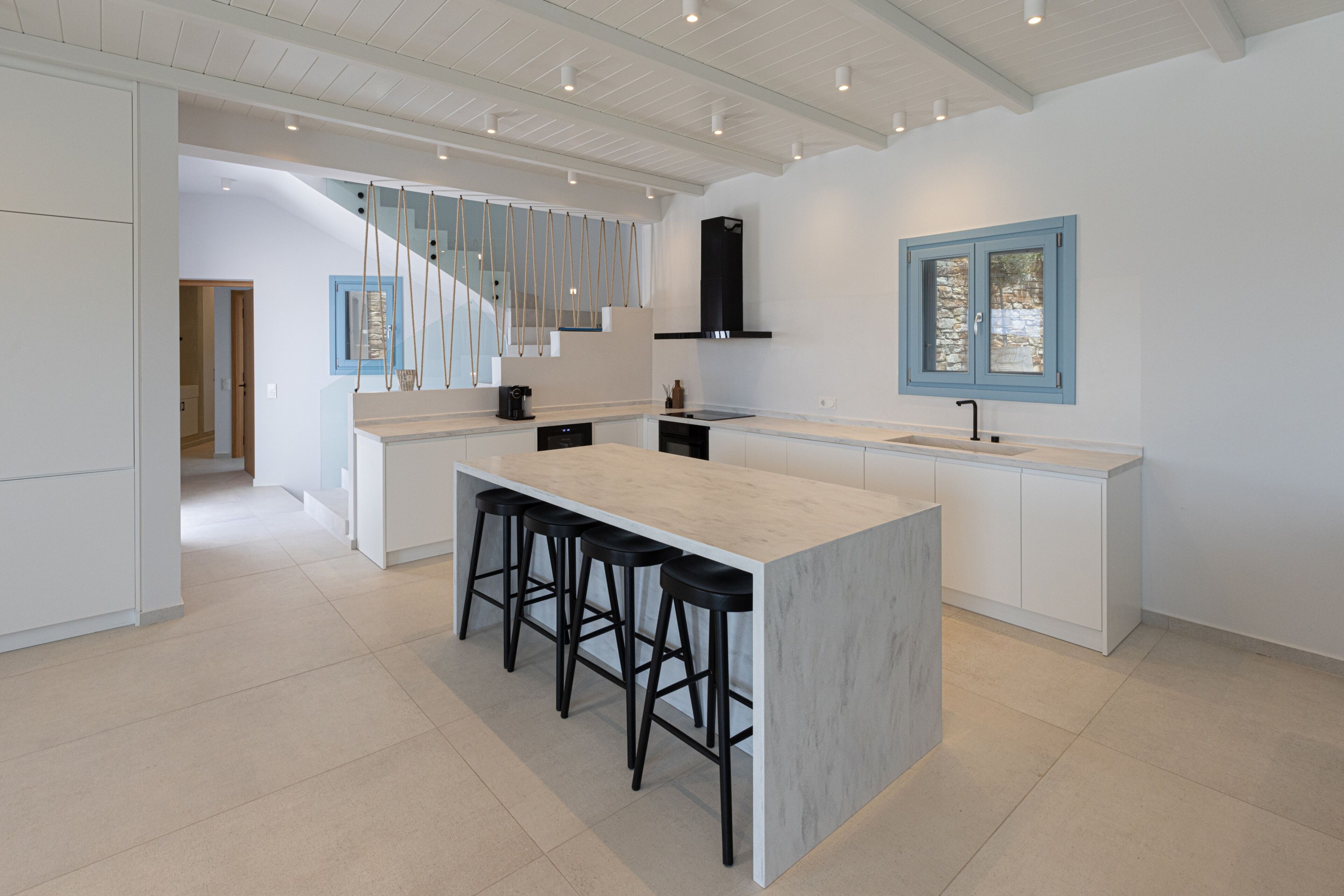 Una cucina moderna con isola in marmo, sgabelli da bar neri e lavastoviglie integrata.
