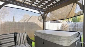 A covered outdoor seating area with a hot tub and a striped sofa. - 5 star Super Host, 3-bedroom, one story,  Hottub Grapevine, Lake Access (Grapevine)