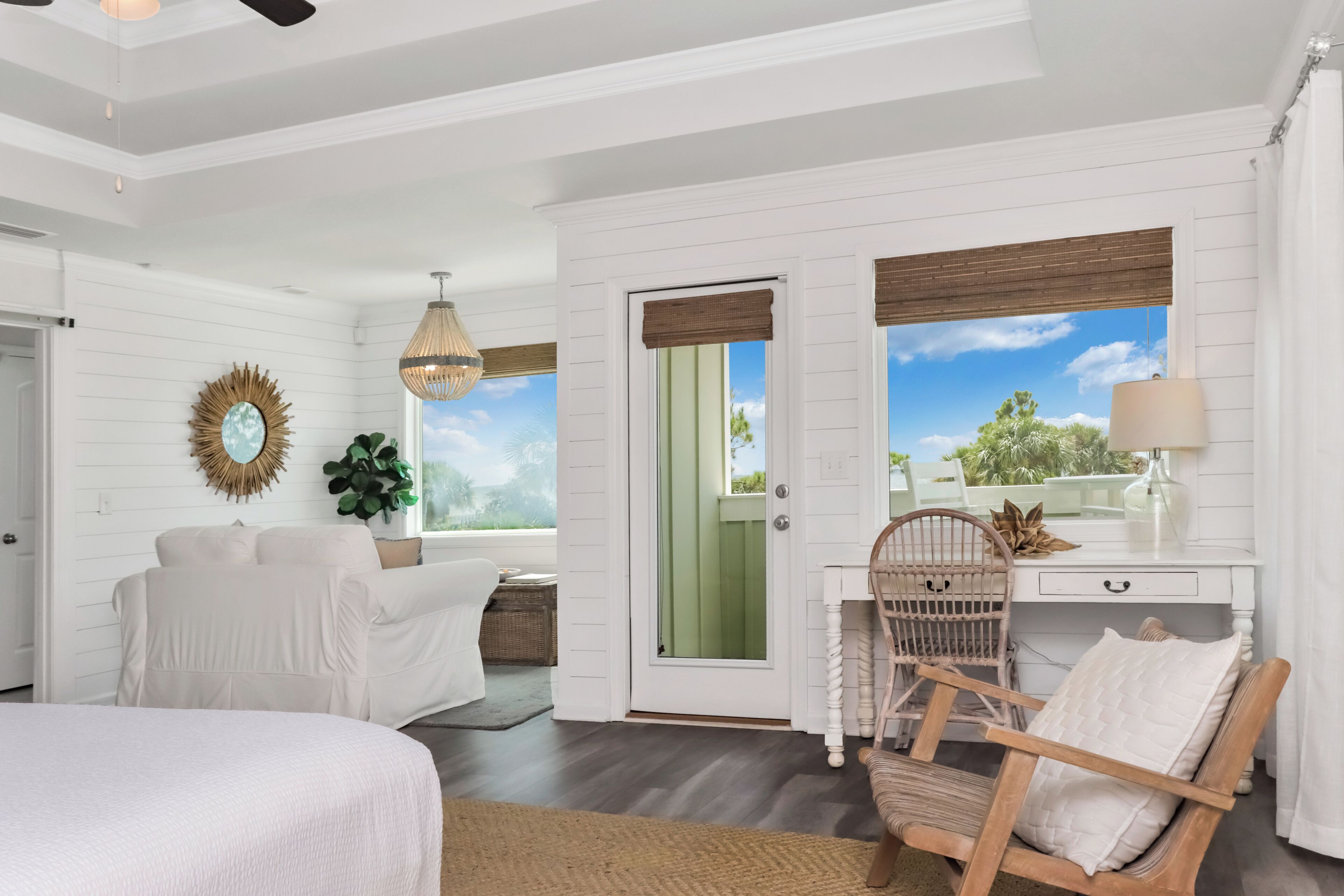 A room with a bed, a desk with a chair, a hanging light fixture, and a view of the outdoors.
