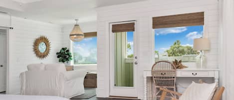 A room with a bed, a desk with a chair, a hanging light fixture, and a view of the outdoors.