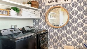 Una sala de lavandería con dos lavadoras, un espejo y un letrero que dice 'LAUNDRY CO. WASH, DRY, & FOLD'.