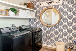 A laundry room with two washing machines, a mirror, and a sign that reads 'LAUNDRY CO. WASH, DRY, & FOLD.' - 🌊 Arlanymor | Windmark Beach | Private Pool, Volleyball + Beach Access (Windmark)