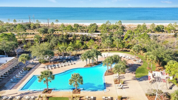 Un resort con una piscina grande, sillas de descanso y vista al océano.