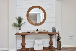 Een houten console tafel met een spiegel erboven, een potplant, decoratieve objecten en een handdoek op de vloer.