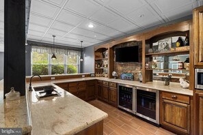 A kitchen with a stone backsplash, wooden cabinets, a built-in oven, and a large window with blinds. - The Whispering Lane Estate Luxury 4BR (Montoursville)