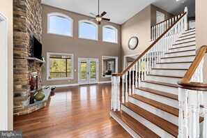 A spacious interior with a wooden staircase, a stone fireplace, and large windows. - The Whispering Lane Estate Luxury 4BR (Montoursville)