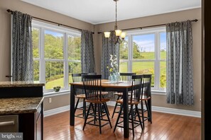 A dining area with a table and chairs, large windows with curtains, and a view of greenery outside. - The Whispering Lane Estate Luxury 4BR (Montoursville)