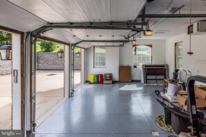 An open garage with a concrete floor, a wooden ceiling, and a metal door. - The Whispering Lane Estate Luxury 4BR (Montoursville)