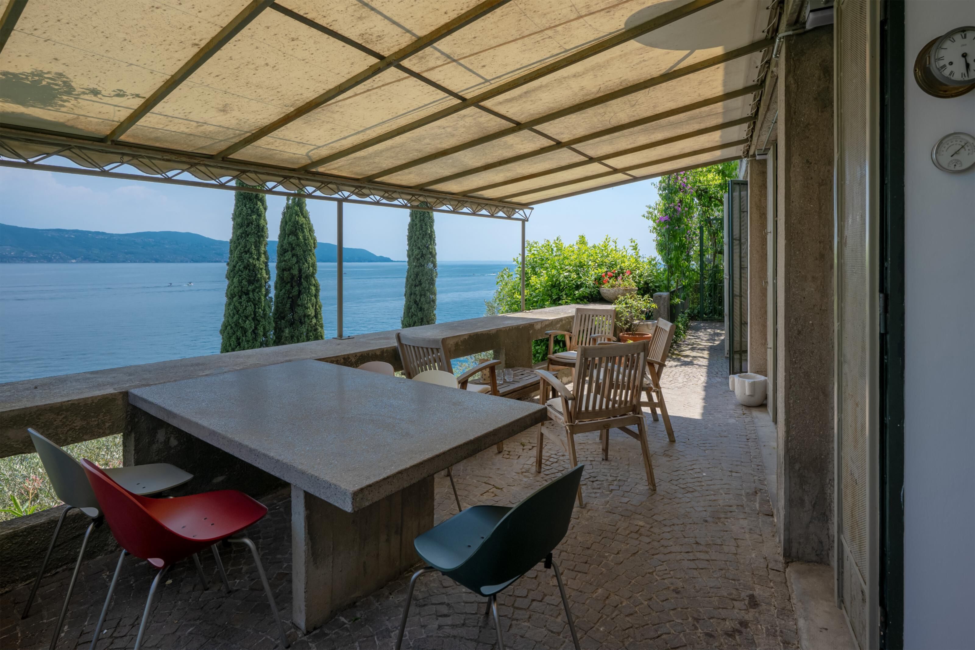 Een terras buiten met een tafel en stoelen, met uitzicht op water en heuvels.