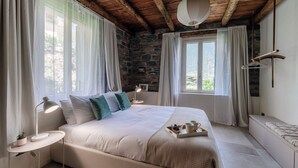 Ein Schlafzimmer mit Stehwand, einem Bett mit weißer Bettwäsche, zwei Nachttischen mit Lampen und Blick ins Freie.