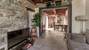 Ein Zimmer mit Steinwänden, einem Fernseher, einer Couch, einem Essbereich mit Stühlen und einer Pflanze.