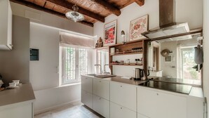 Eine Küche mit weißen Schränken, einer Edelstahl-Spüle, Holzregalen und einem Fenster mit Blick.