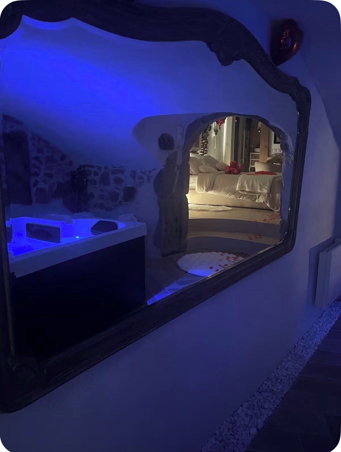 Una habitación con pared de piedra, cama con ropa de cama blanca y una pequeña mesa con lámpara.