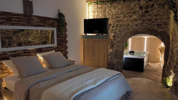 Un dormitorio con pared de piedra, cama, televisor y zona de spa.
