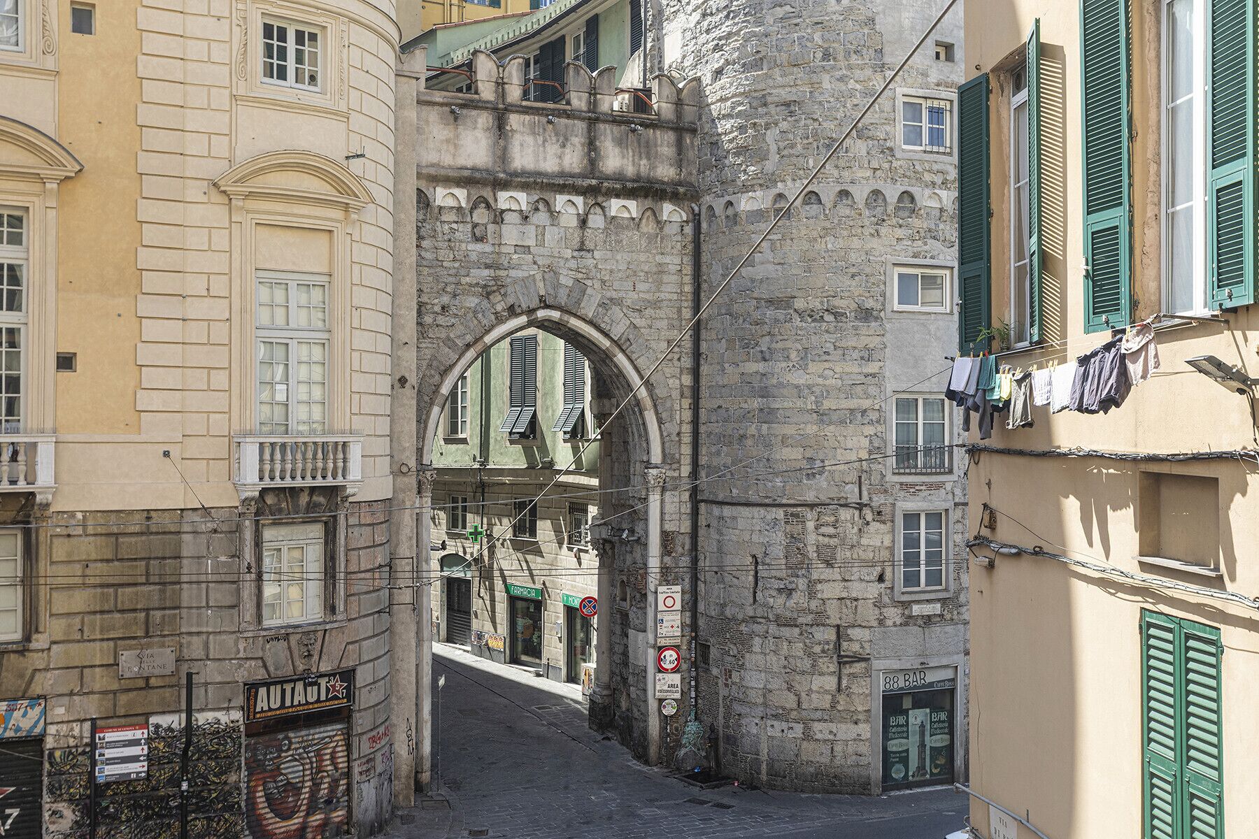 Une rue étroite bordée d’immeubles historiques en pierre, avec une arche bien visible et un bar au bout.