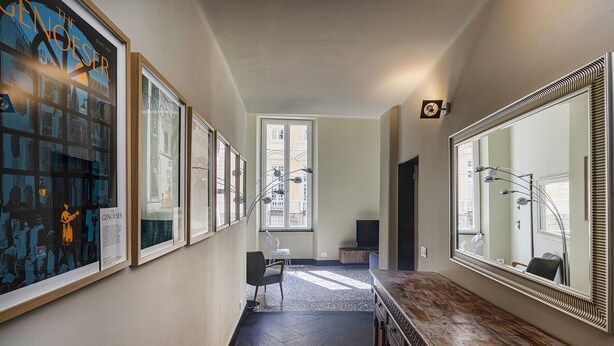 Ein Flur mit gerahmten Kunstwerken, einem großen Spiegel und einer Sitzecke mit Sessel und Tisch.