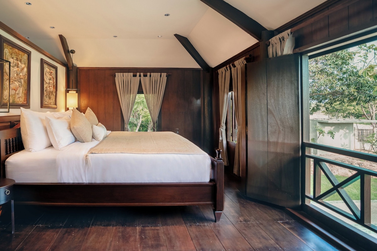 A large bed with white linens, wooden headboard, and a nightstand with a lamp.